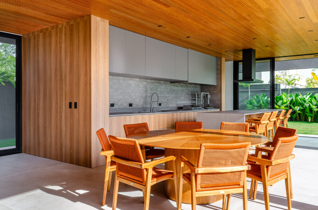 Área gourmet com mesa redonda, marcenaria em madeira e vista para o jardim – Casa Sintonia