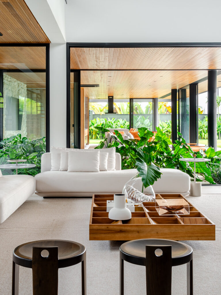 Sala de estar integrada ao jardim interno, com sofá branco e mesa de centro em madeira – Casa Sintonia