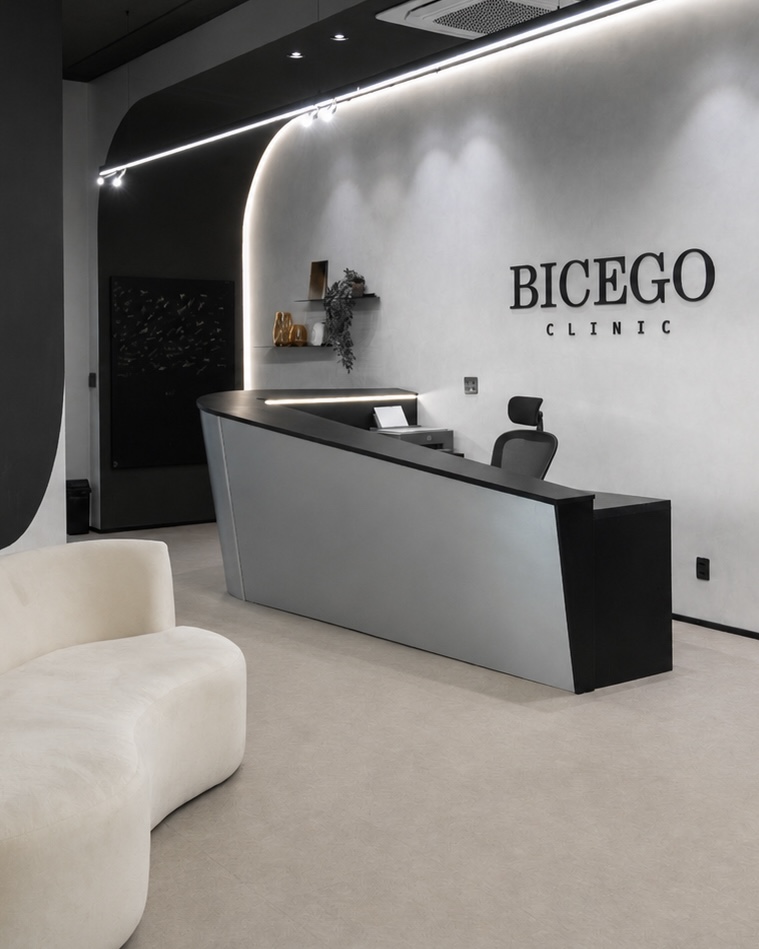 Recepção com balcão escuro inclinado, sofá orgânico branco e logo Bicego na parede – Bicego Clinic