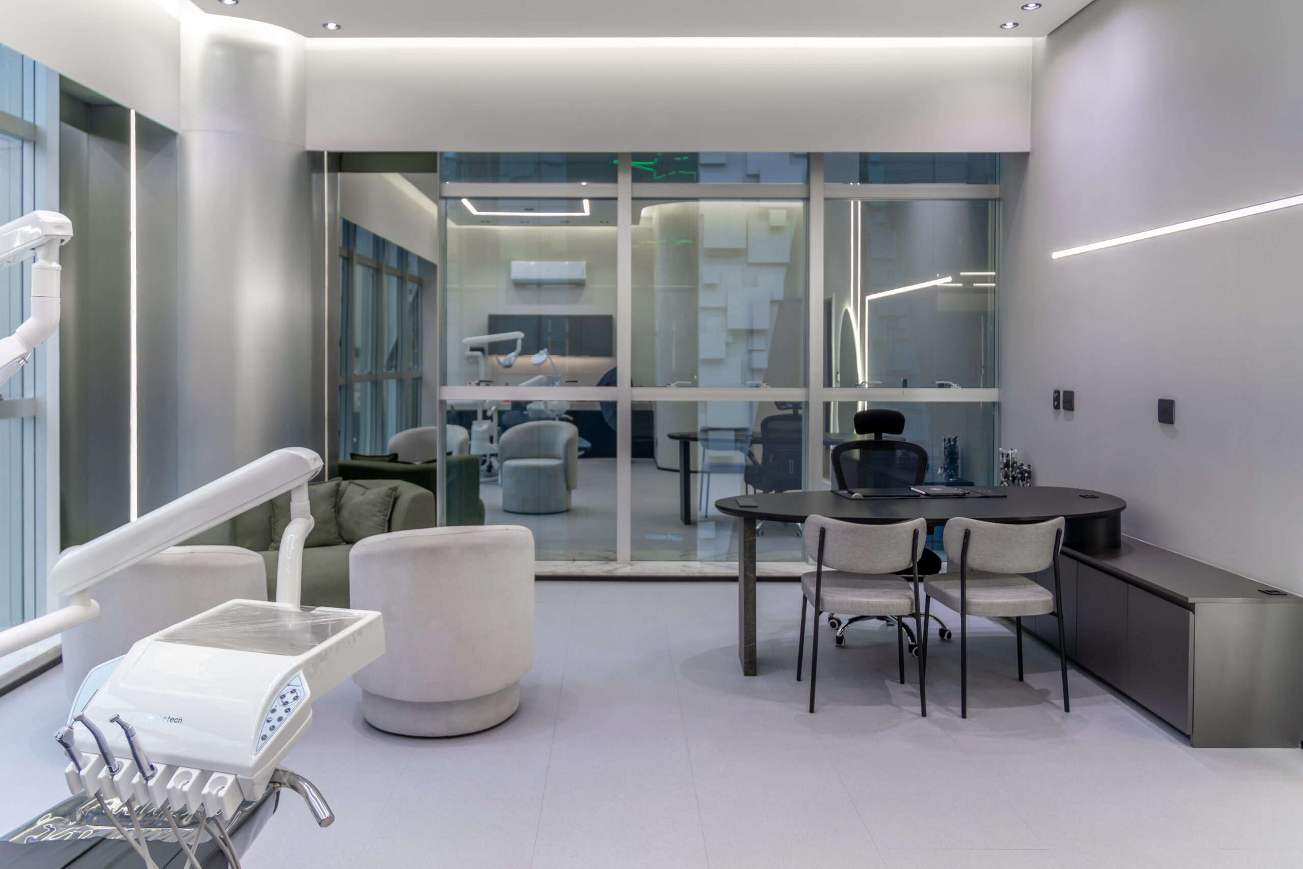 Consultório odontológico amplo com mesa escura, poltronas e divisória de vidro para a área de espera – Bicego Clinic